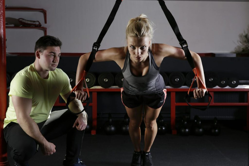 A woman performing strength training with a trainer in a gym setting, showcasing fitness and dedication.